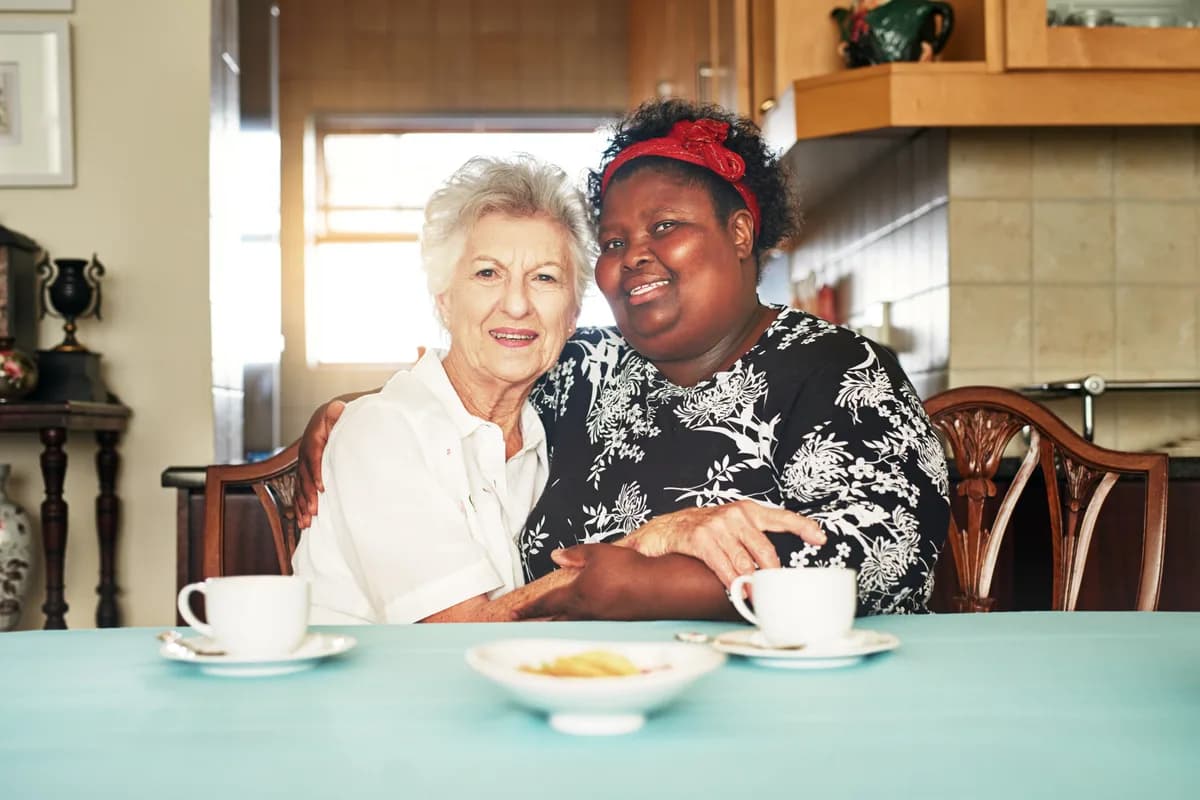 Caregiver sharing tea with an elderly woman at her kitchen table